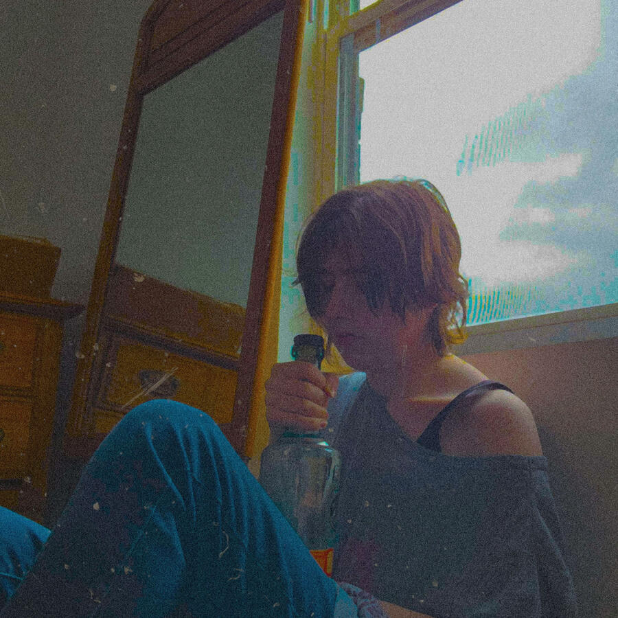Twilight sitting against a window holding a bottle of vodka. She has a sad look on her face while staring at the bottle.